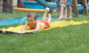 Enfant qui joue en glissant sur de l'eau. Le terrain étant installé sur du gazon synthétique